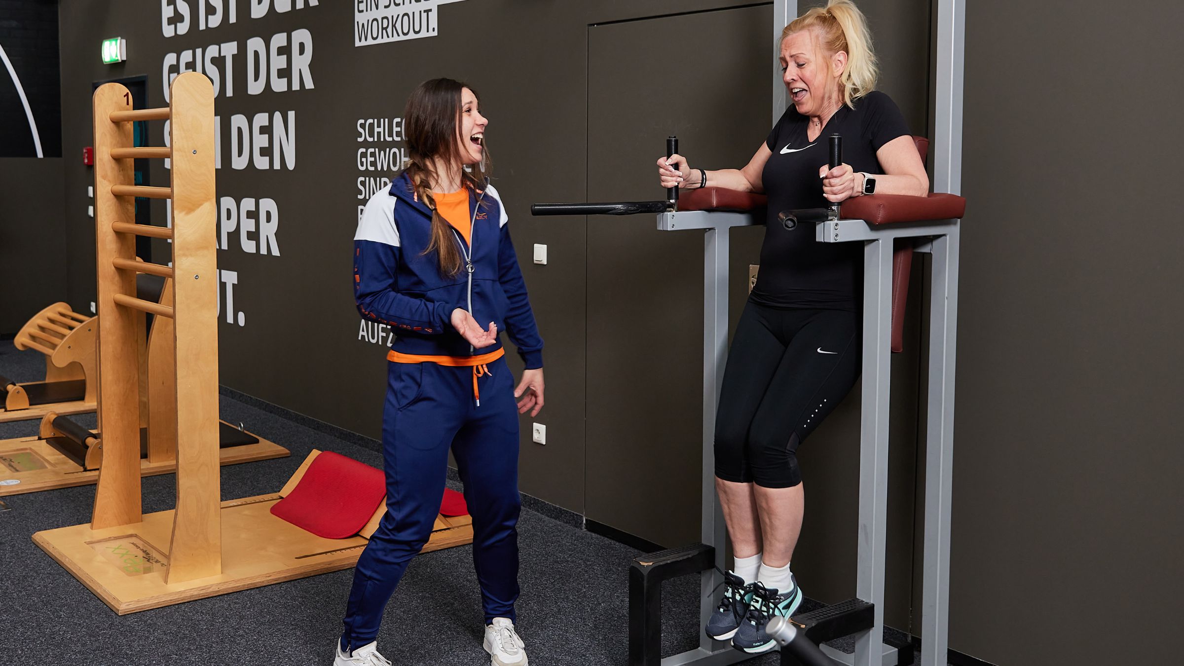 Ein Frau wird von einer Trainerin bei einer Bauchübung an einem Kniehebe-Gerät im INJOY Fitnessstudio Bregenz betreut.