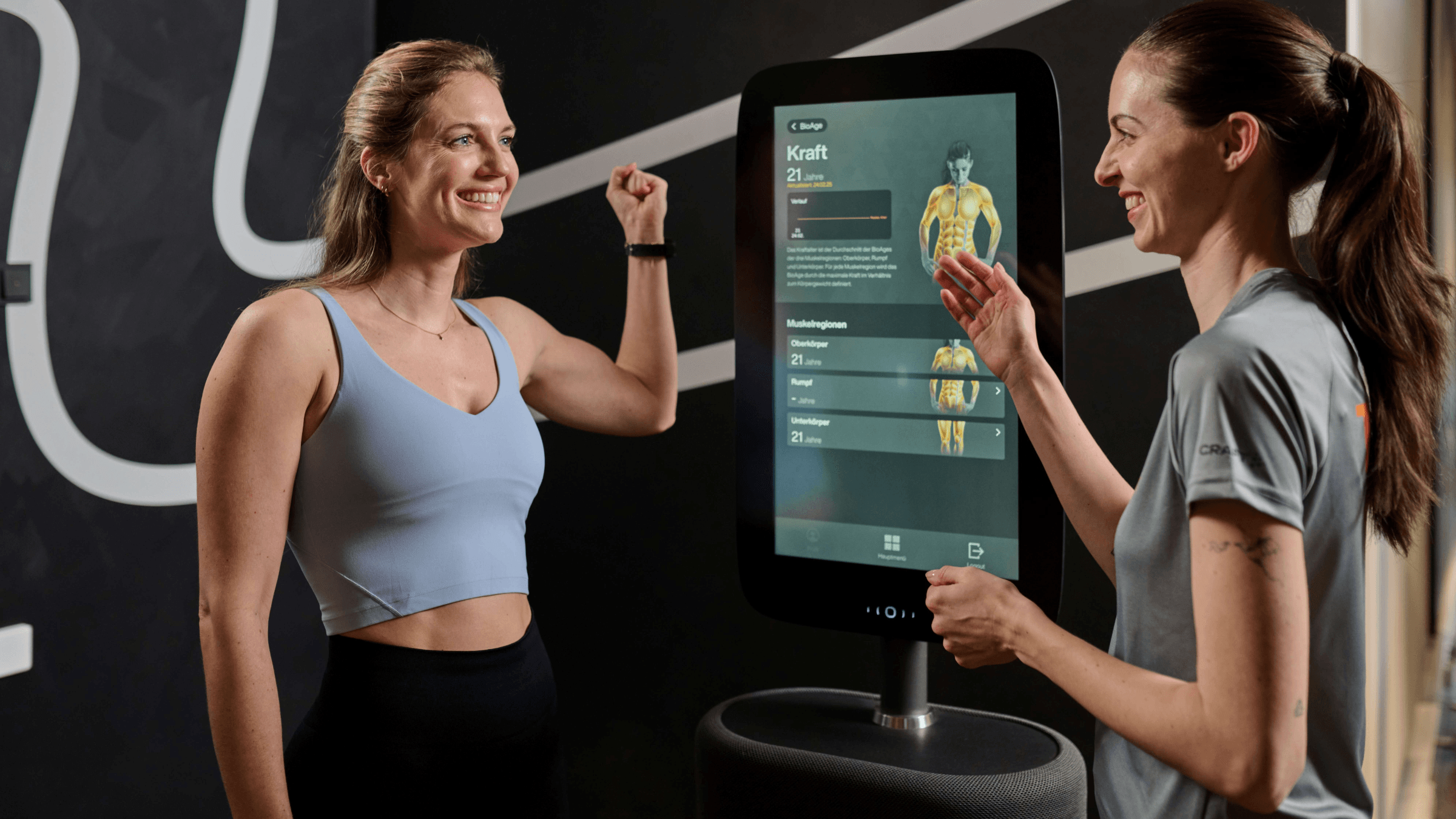 Eine Trainerin und ein INJOY Mitglied stehen am BioAge Terminal im Fitnessstudio.