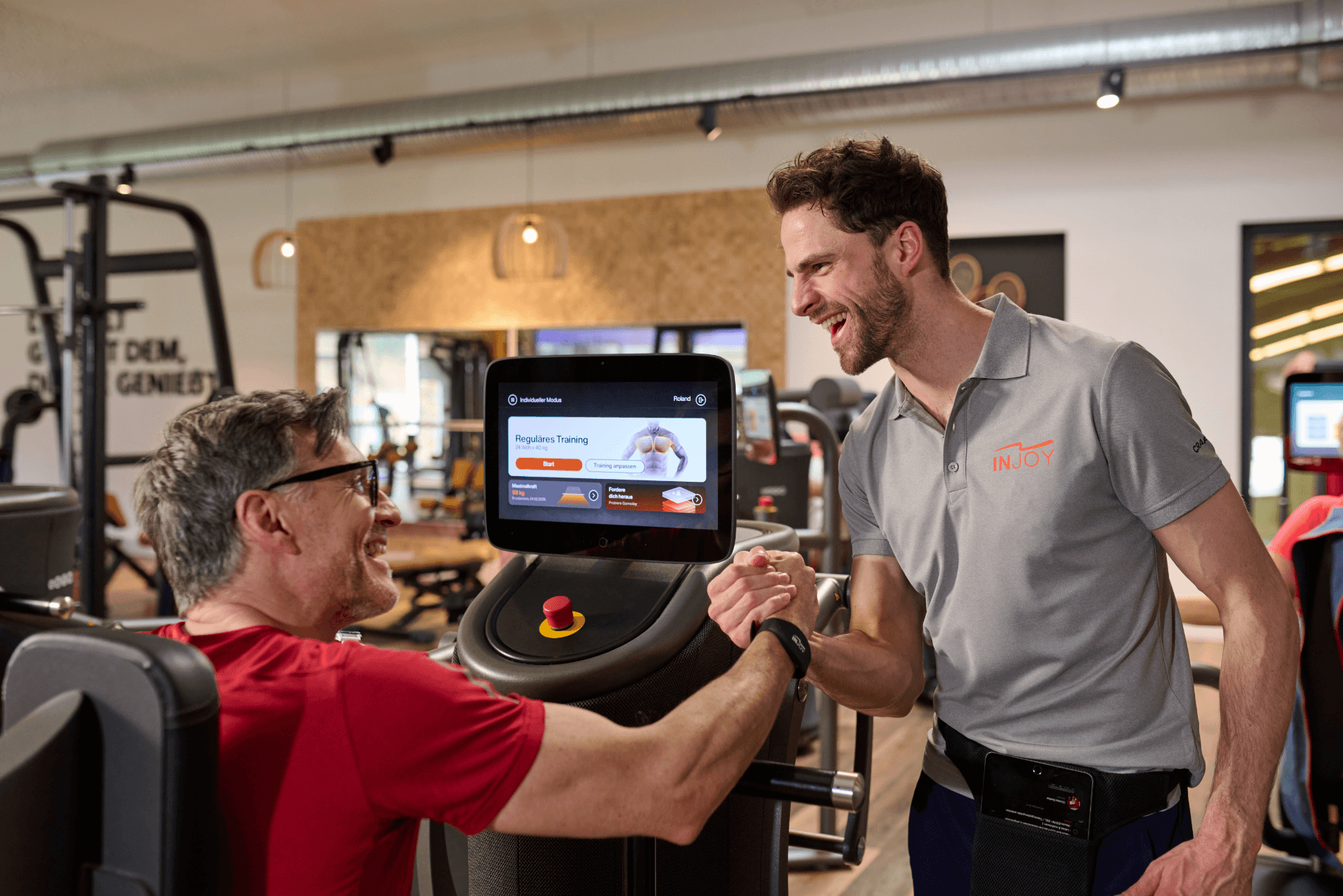 Ein INJOY Trainer klatsch mit einem männlichen Mitglied ein, welches an einem EGYM Gerät trainiert.
