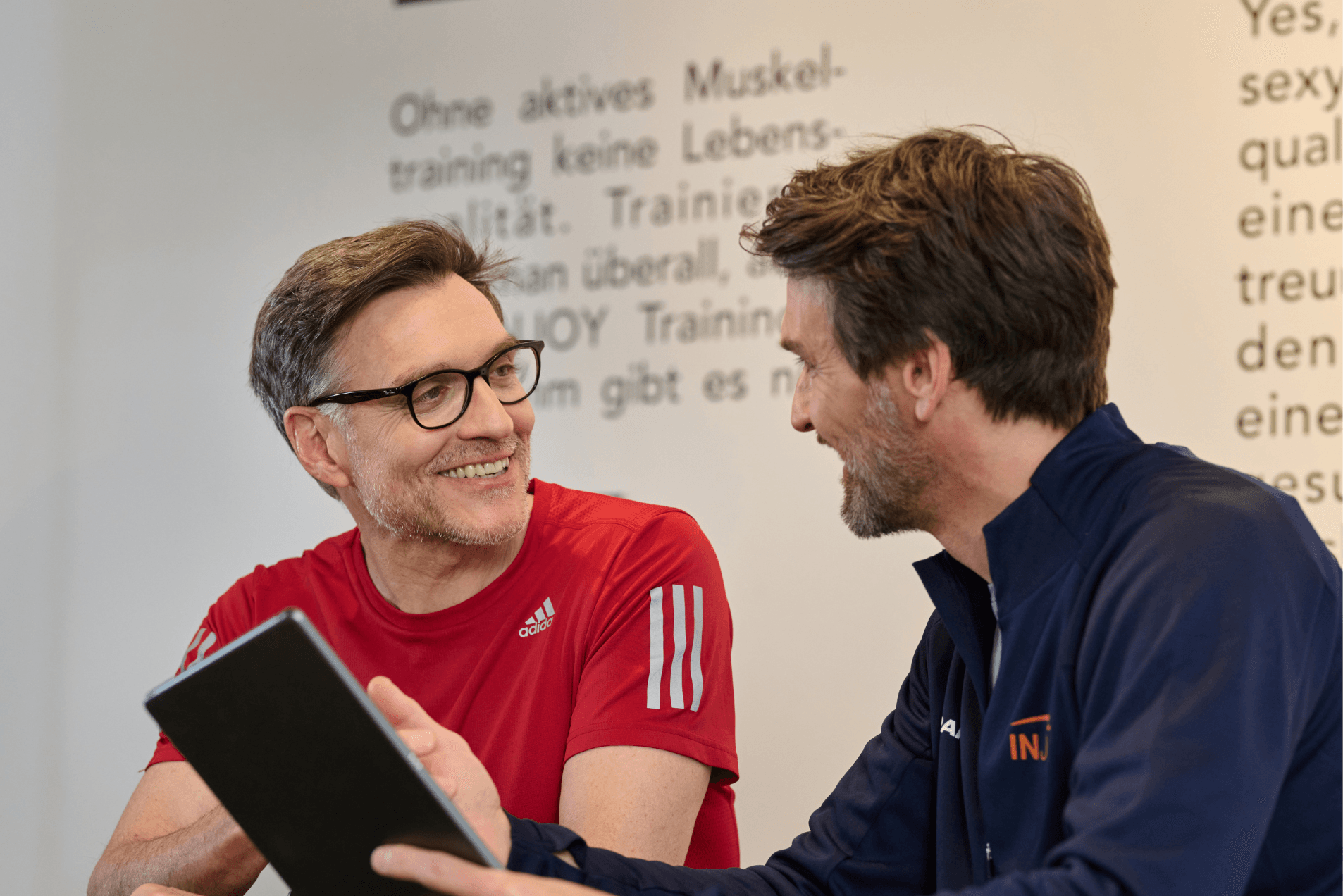 Ein männlicher INJOY Trainer erklärt einem Mitglied die INJOY 360 App.