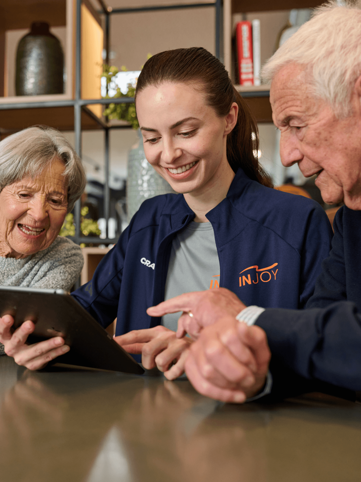 Eine junge INJOY Trainerin erklärt einem älteren Ehepaar die INJOY App auf einem iPad.