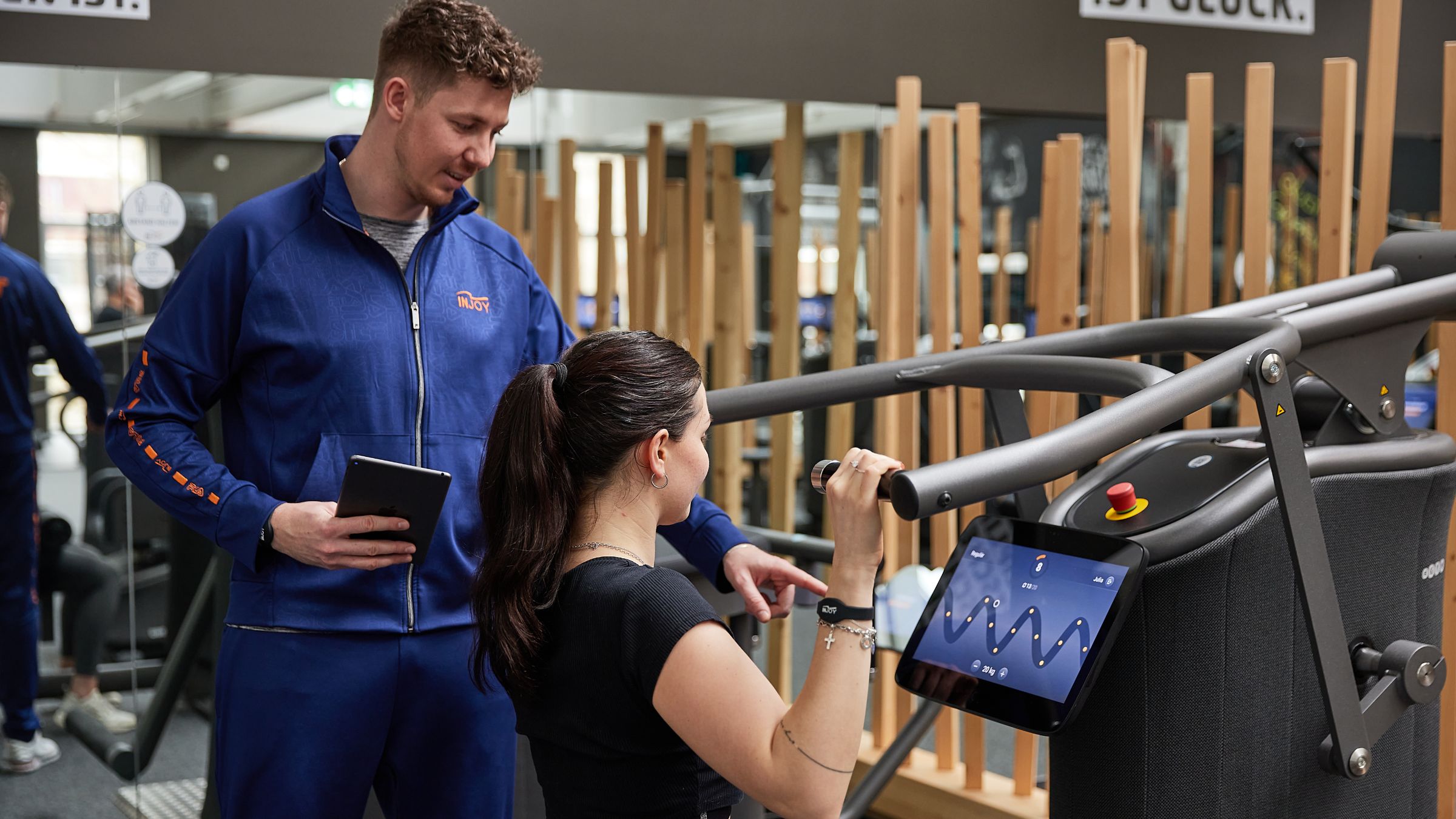 Ein Trainer erklärt einem Mitglied eine Übung am Latzug-Kraftgerät im INJOY Fitnessstudio Bregenz.