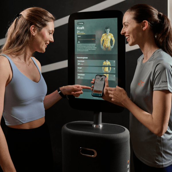 Ein blonde, attraktive Dame wird von einer INJOY Mitarbeiterin vor einem digitalen Screen beraten.