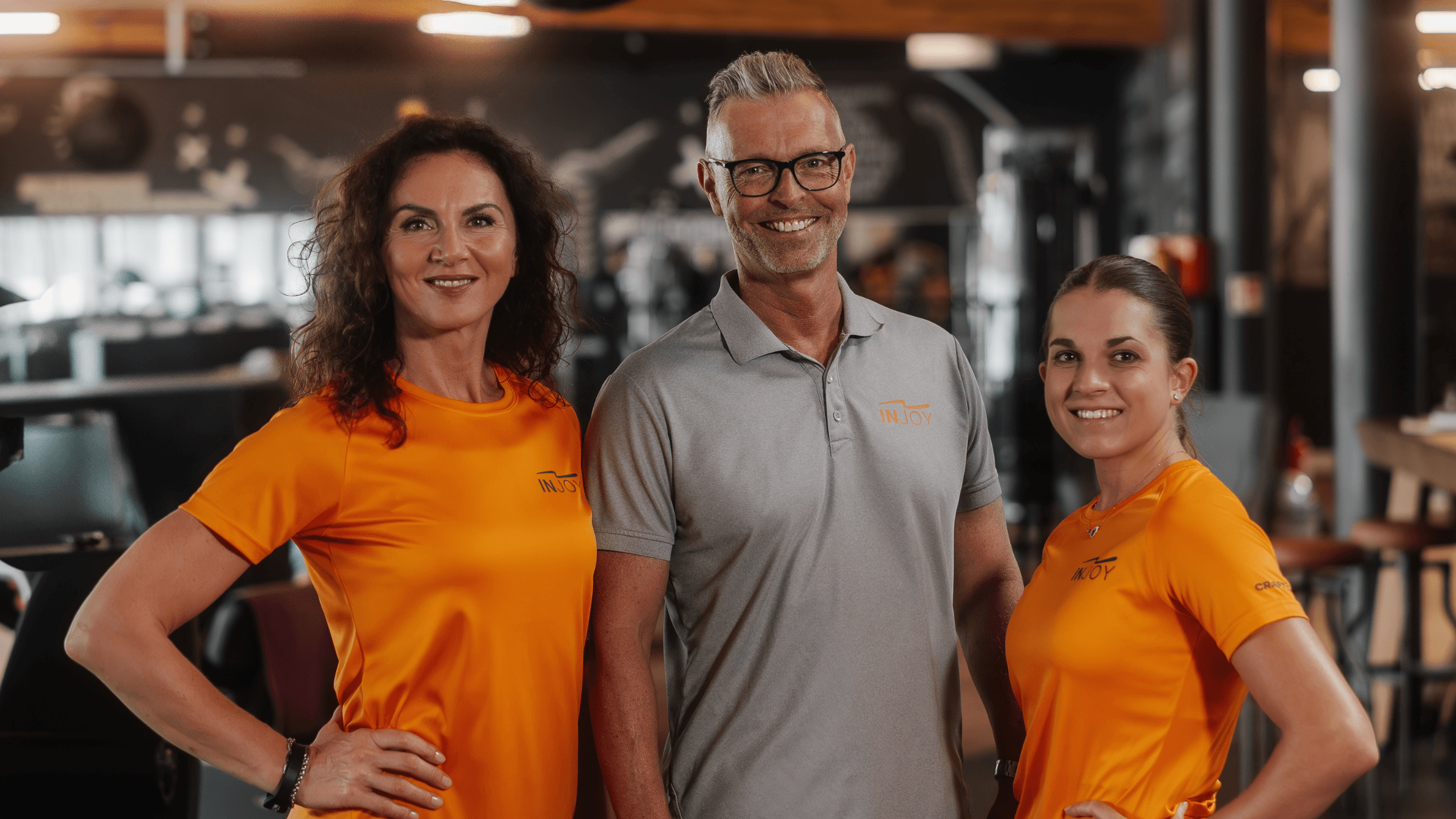Gruppenfoto von drei lächelnden Mitarbeitern im INJOY Fitnessstudio Hallwang.