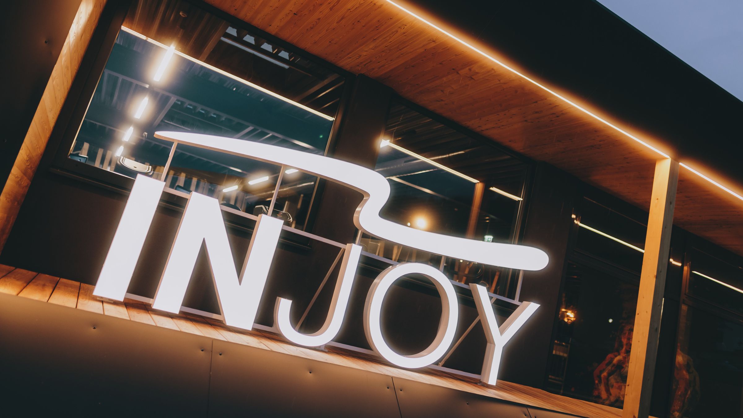 Außenansicht mit einem leuchtenden INJOY-Logo vom INJOY Fitnessstudio Kaprun.