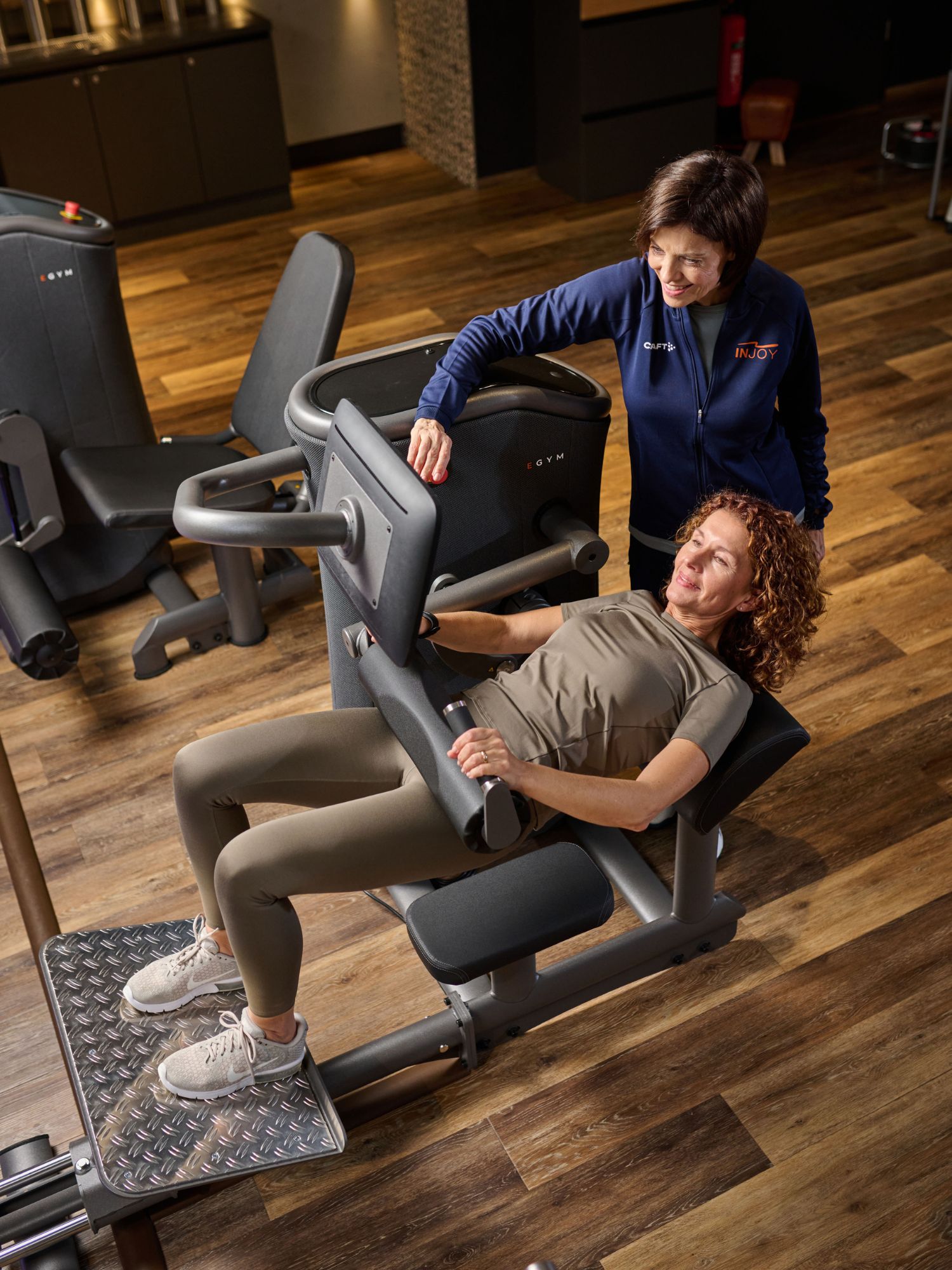 Frau trainiert auf Hip-Thrust-Gerät mit Betreuung durch eine INJOY Mitarbeiterin