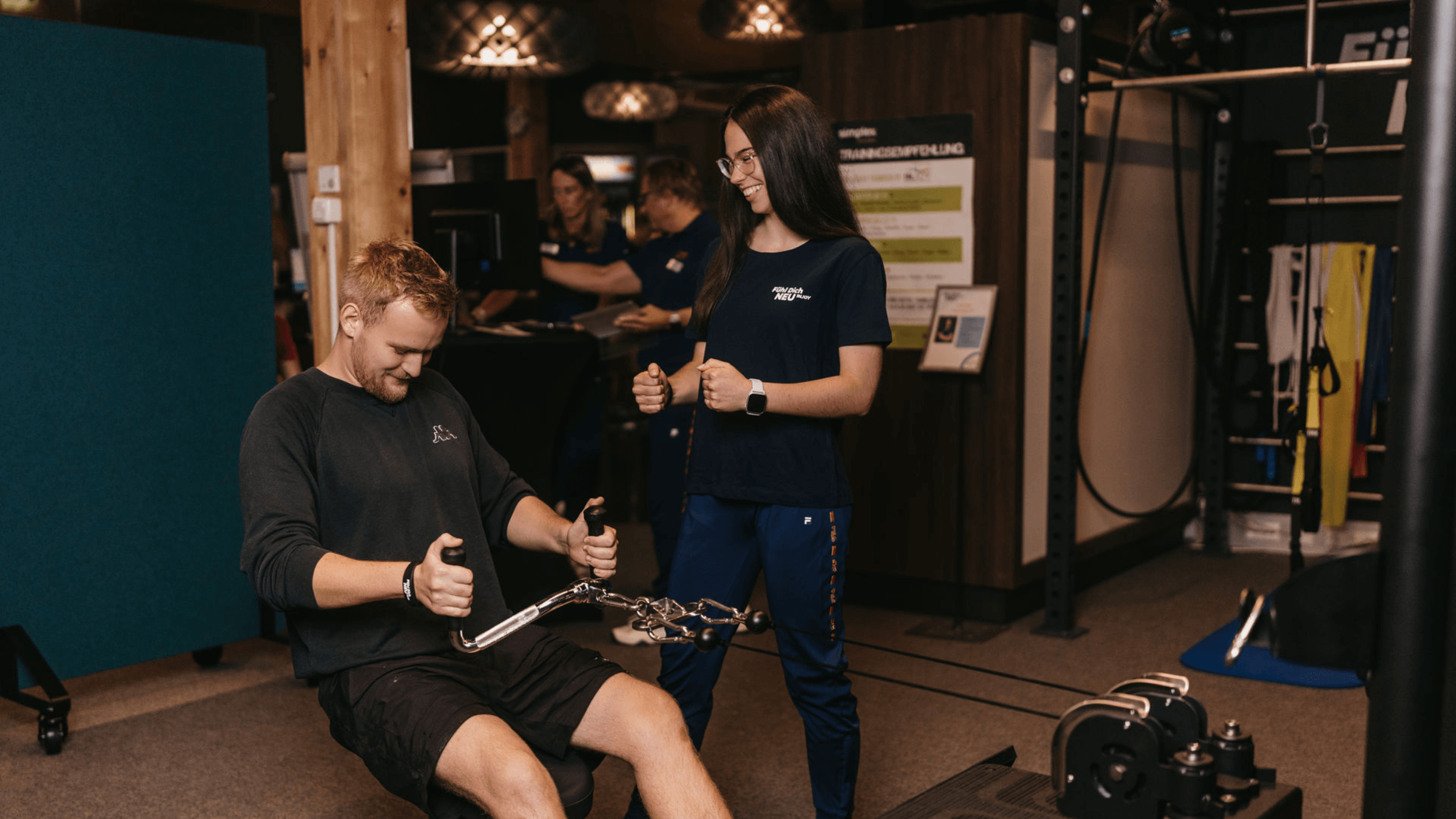 Eine Trainerin betreut einen Mann bei einer Übung am Ruder-Kraftgerät im INJOY Fitnessstudio Eferding.