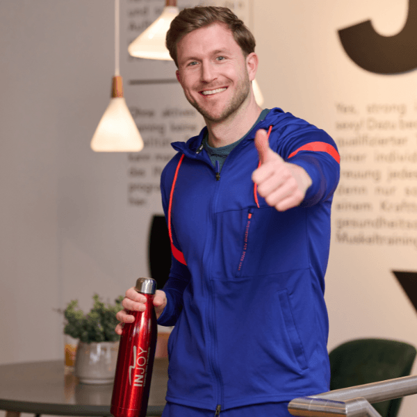 Ein jüngeres INJOY Mitglied mit INJOY Flasche in der einen Hand und einem Daumen nach oben mit der anderen Hand.