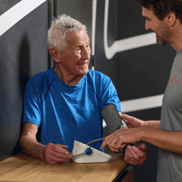 Ein INJOY Trainer misst bei einem älteren Mitglied den Blutdruck.