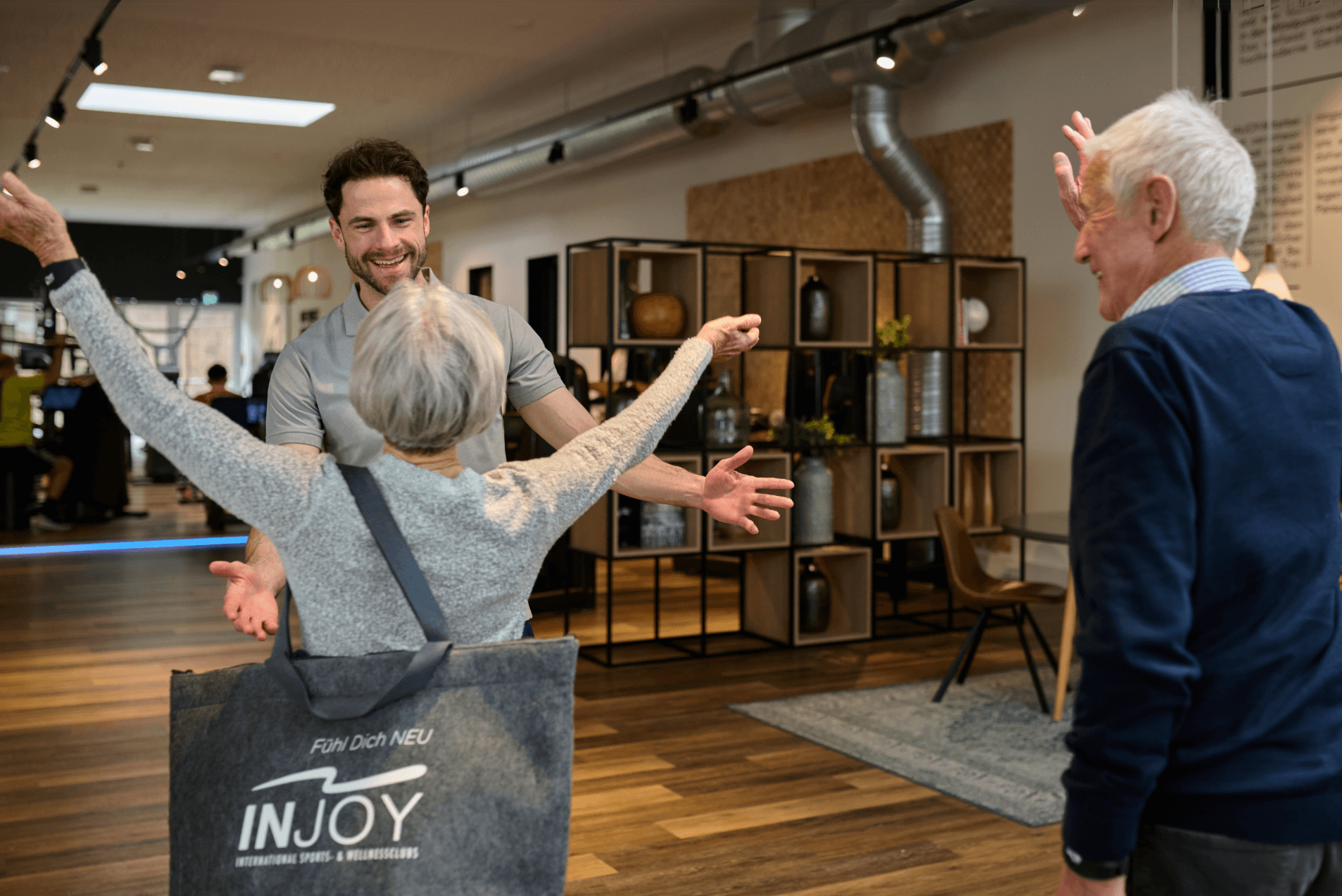 Zwei ältere INJOY Mitglieder werden herzlich von einem INJOY Trainer in Empfang genommen