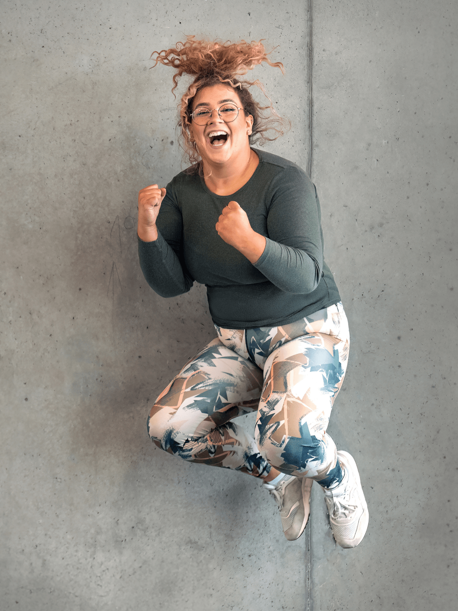 Ein INJOY Fitnessstudio-Mitglied springt vor Freude in die Luft und lacht dabei in die Kamera.