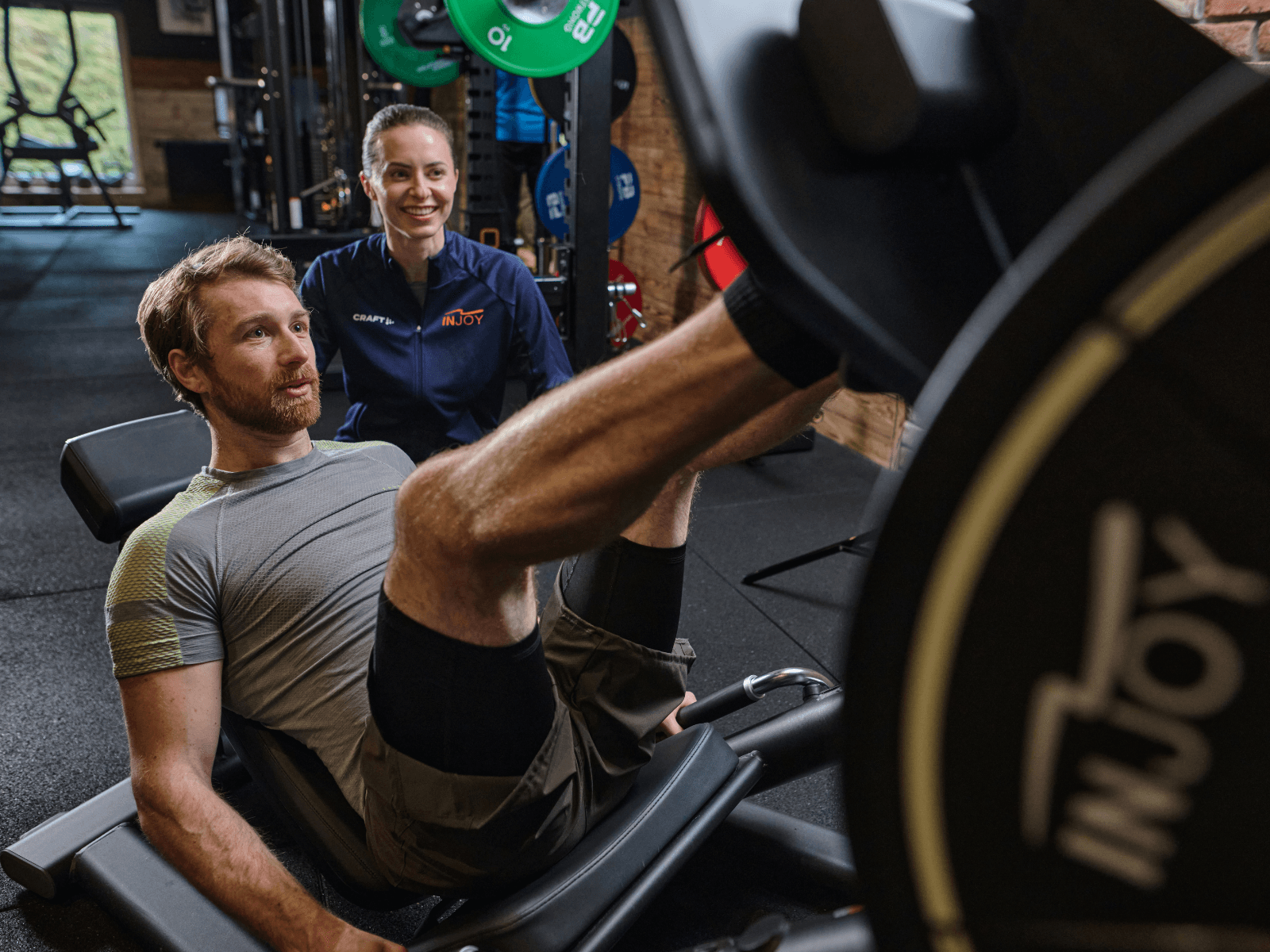 Mitglied trainiert konzentriert an einer Beinpresse und erhält Unterstützung einer INJOY Trainerin – steht für effektives, wissenschaftlich qualifiziertes Muskeltraining bei INJOY.