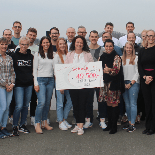 Die INJOY Österreich Franchisenehmer posieren gemeinsam für ein Gruppenbild. Es wird ein großer Spendenscheck stolz in die Kamera gehalten.